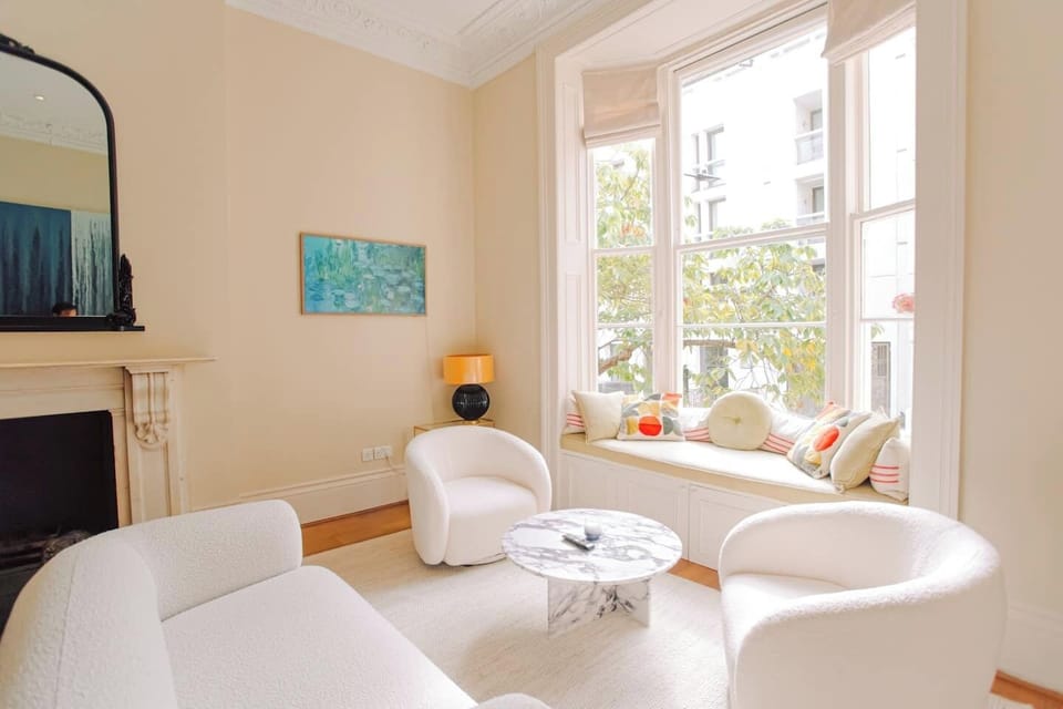 A cozy seating area with white chairs, a marble coffee table, and a window bench with cushions.