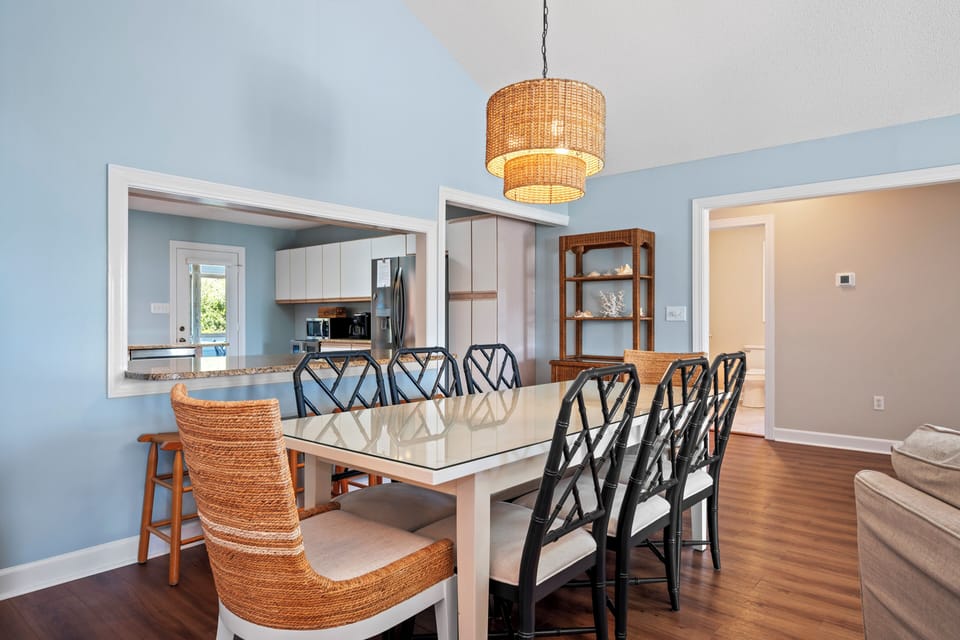 Gather around your elegant dining table where wicker lighting and coastal chairs create the perfect setting for memorable meals together.