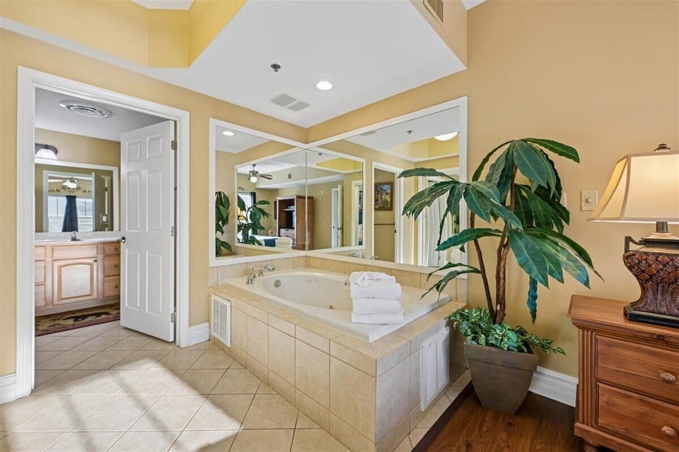 Unwind in your spa-like bathroom featuring a spacious jetted tub surrounded by warm tones and tropical greenery for ultimate relaxation.