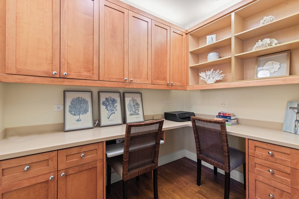 Your dedicated workspace awaits with warm wood cabinetry, built-in storage, and charming coastal artwork to inspire productive moments.