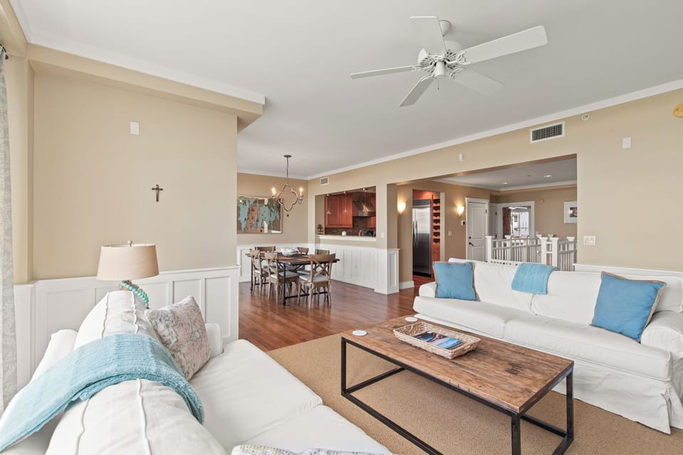 Settle into plush white sofas adorned with coastal blue pillows in this airy open-plan space where hardwood floors flow seamlessly from living to dining.