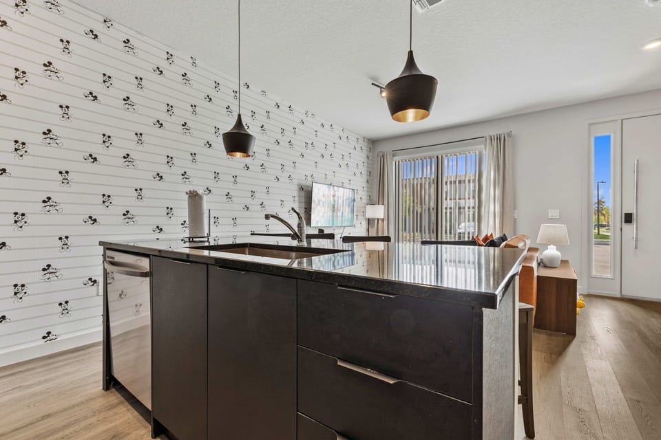 Modern kitchen island with black granite countertop and playful mickey mouse wallpaper in the background