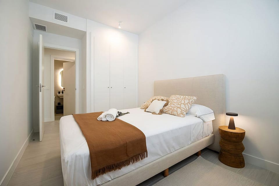 Relax in a serene bedroom with crisp linens and warm wooden accents. A sleek en-suite bathroom awaits just beyond the door.
