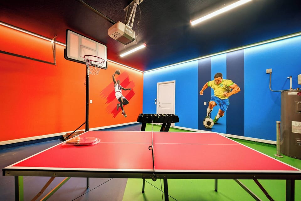 Experience a lively game room with a striking red ping pong table and vibrant orange and blue walls decorated with energetic sports murals, creating the perfect setting for friendly competition and laughter.