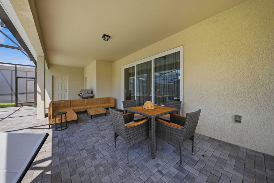 Step outside to a charming outdoor seating area with a stylish table and comfortable wicker chairs, perfect for al fresco dining, while sleek pavers guide you to large glass doors for a seamless indoor-outdoor experience.