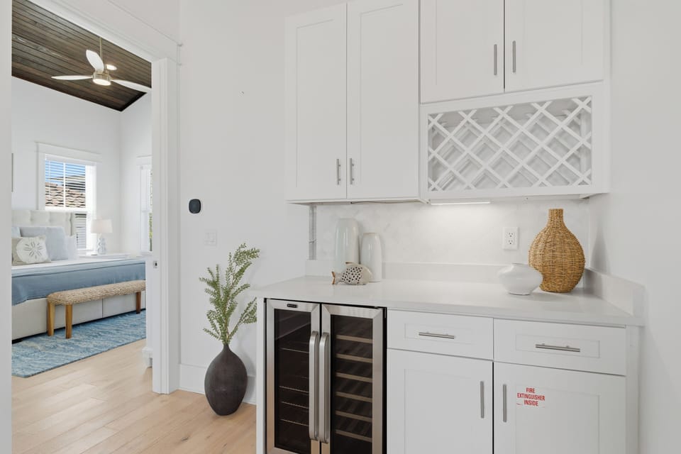 Your private wine station features elegant white cabinetry, dual temperature zones, and charming coastal touches for perfect entertaining.