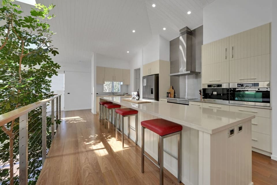 Contemporary kitchen featuring spacious island, red cushioned bar stools, and modern appliances for family cooking.
