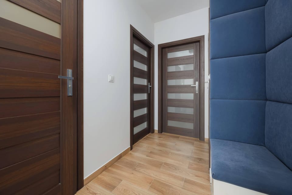 The apartment entryway features dark wood doors and a built-in navy blue upholstered bench for comfort. The space is clean and welcoming, providing a functional transition into the home.