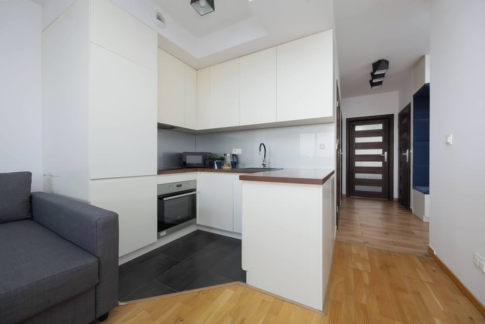 A hallway-to-kitchenette transition demonstrates the seamless integration of the cooking area into the main living space. The light wood flooring continues throughout, providing a cohesive look.
