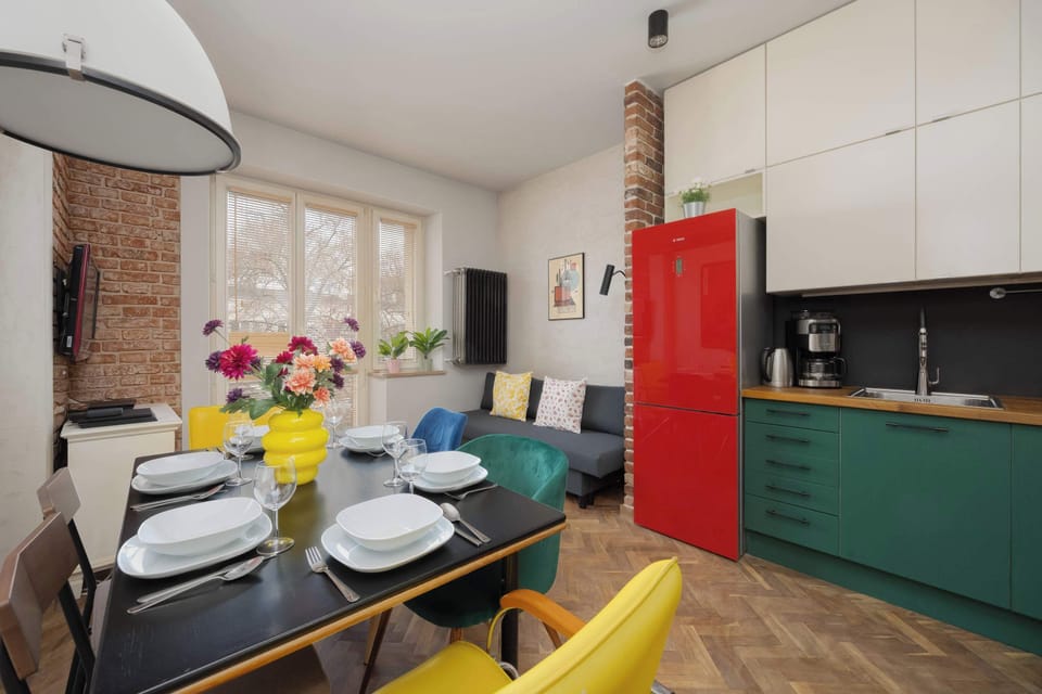 The kitchen transition area features a bold red refrigerator that acts as a focal point between the cooking and living spaces. A dark accent wall with a wall clock adds a sophisticated touch to the layout.