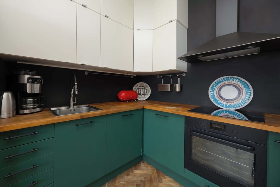 A modern kitchen setup showcases white handleless cabinetry and a dark wood-effect countertop. The space is equipped with an integrated oven and a minimalist black sink.