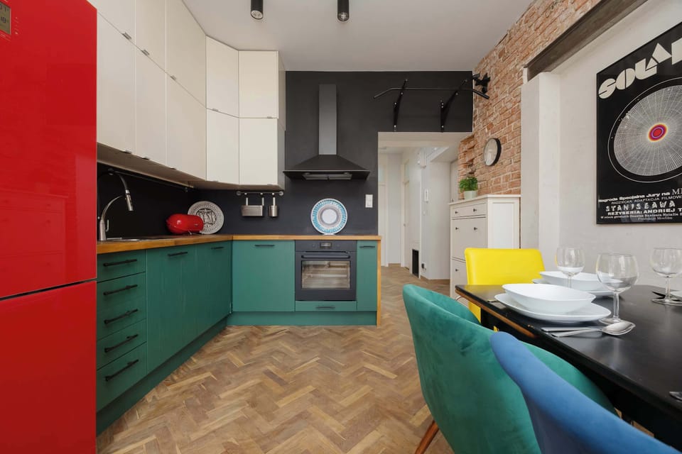 A full view of the L-shaped kitchen highlights the emerald green cabinetry and a black chimney-style extractor hood. The layout is compact yet highly functional, with plenty of counter space for meal prep.