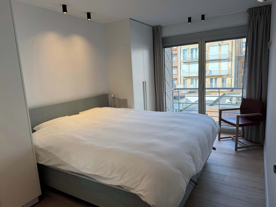 Modern bedroom with natural light from large windows and a balcony view.