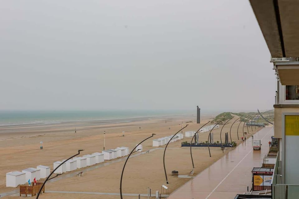 View of the sandy beach with white beach cabins and a paved promenade on a cloudy day