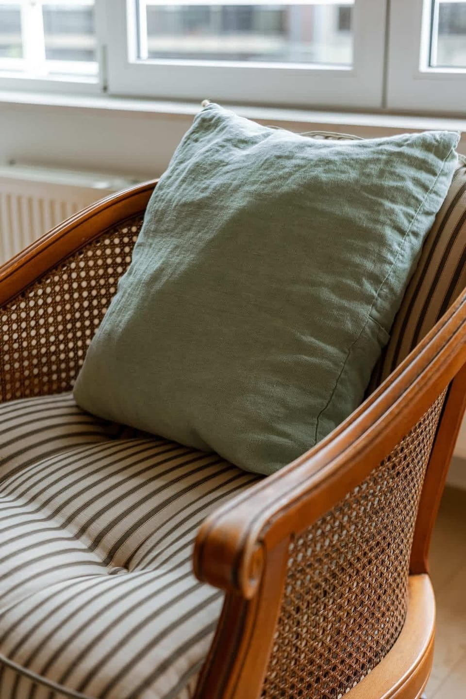 Striped cushioned chair with a green pillow by the window