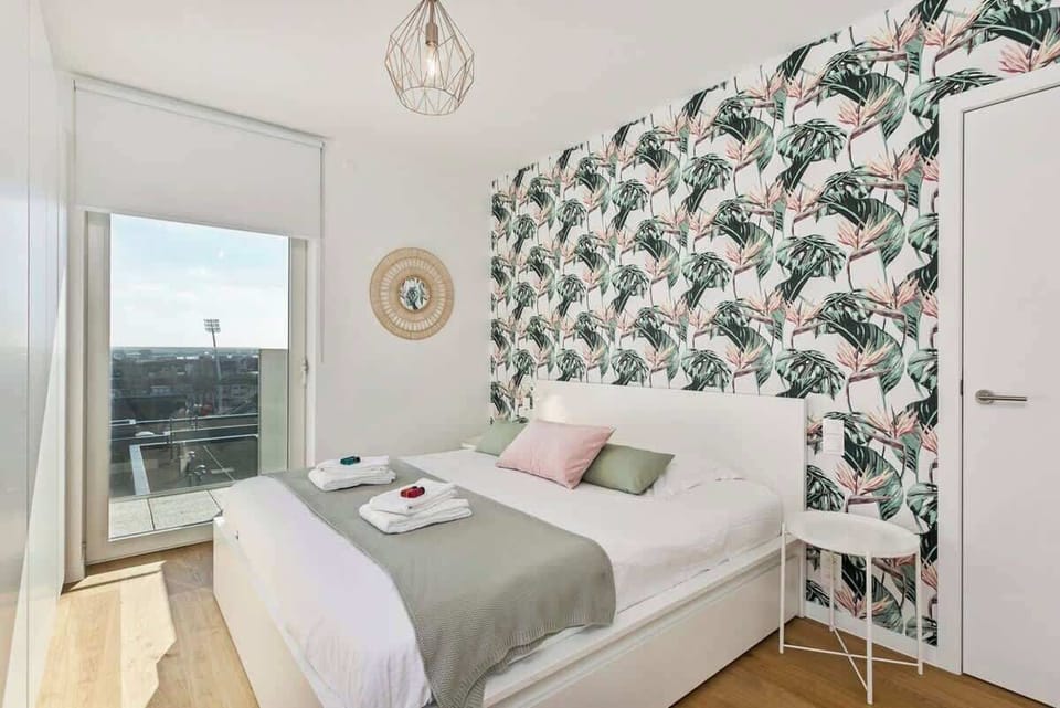 Bright bedroom with tropical wallpaper and city views through a large window