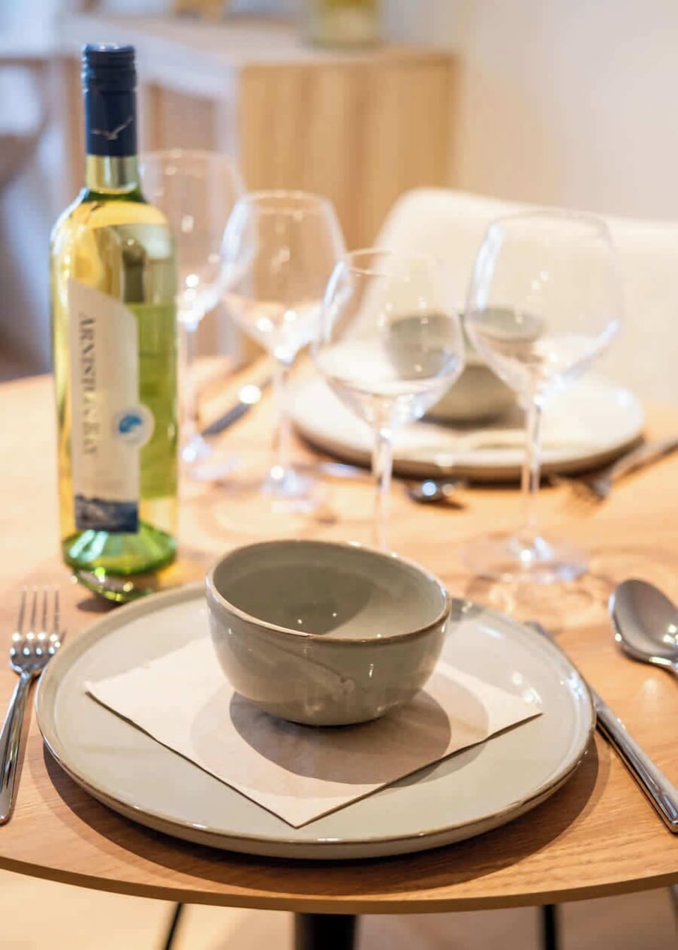 Modern dining table set with ceramic dishes and wine glasses for an inviting meal.