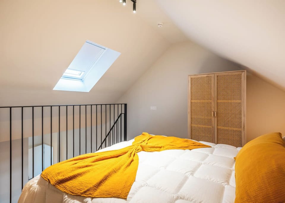 Cozy loft bedroom with natural light from a skylight and warm yellow accents.