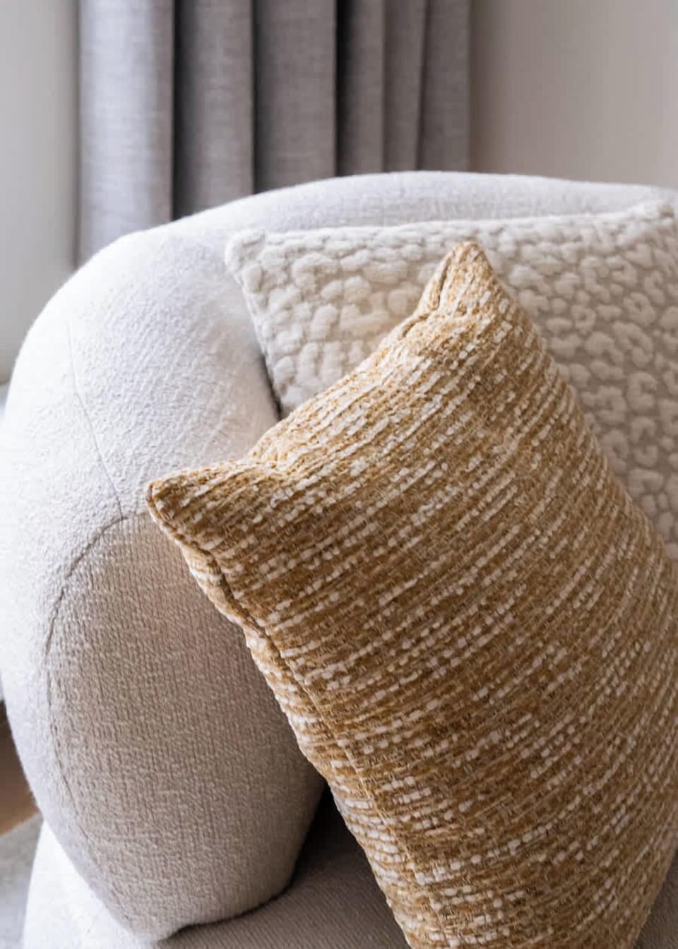 Close-up of a modern textured armchair with decorative cushions in neutral tones.