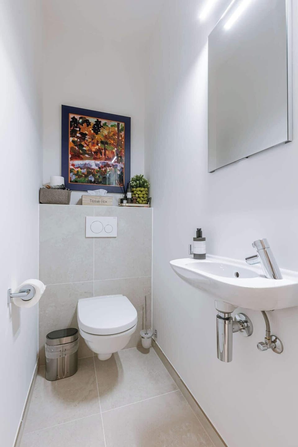 Compact modern bathroom with wall-mounted toilet and decorative artwork
