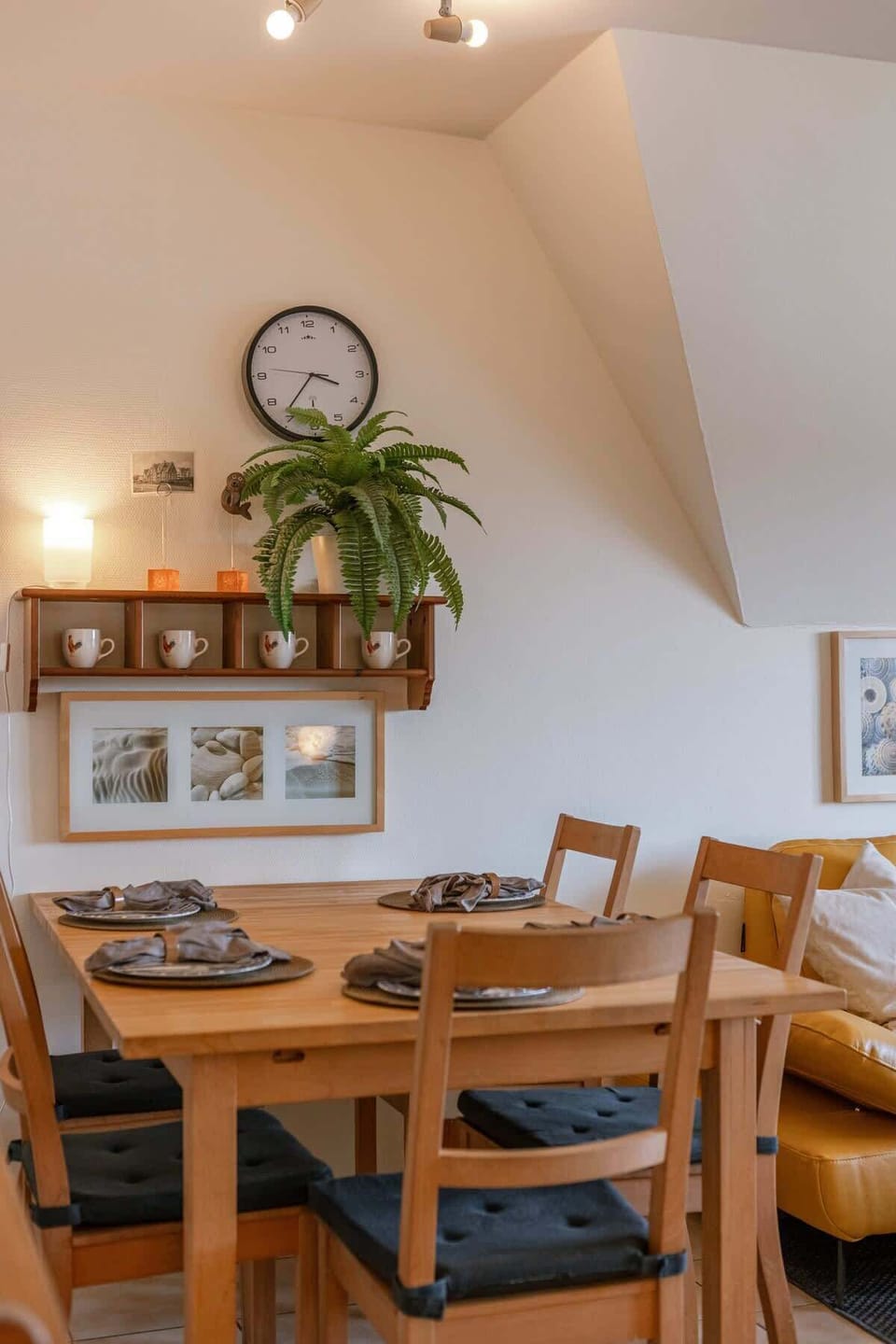Dining area with wooden table, cushioned chairs, and decorative wall shelf with cups and a plant