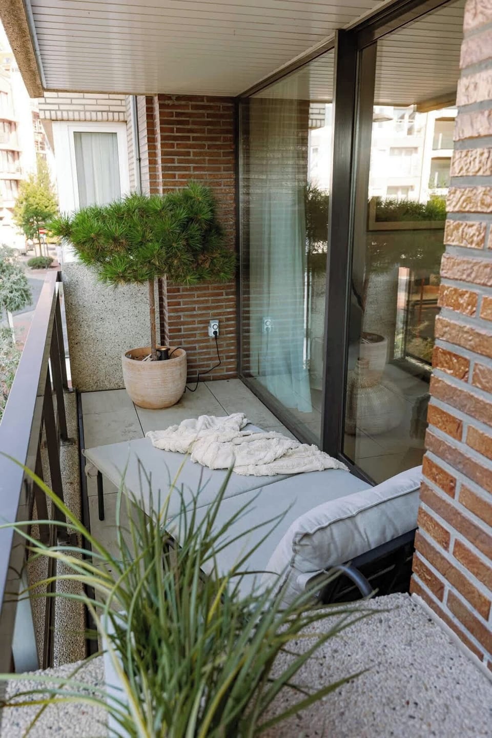 Cozy balcony with cushioned seating and potted plants for relaxing outdoors.