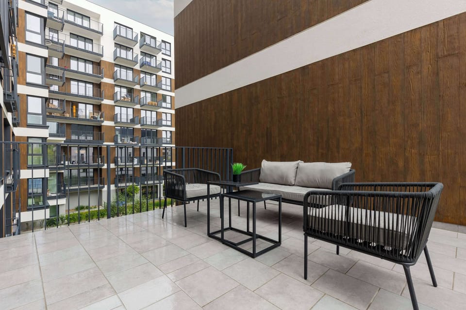 A spacious balcony with outdoor furniture, including a table and chairs, overlooking the complex.