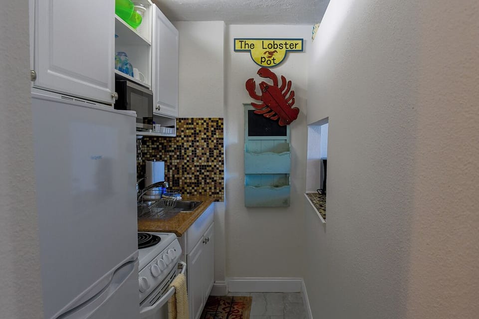 Your galley kitchen features white appliances, mosaic backsplash, and charming coastal touches that make meal prep feel like seaside living.