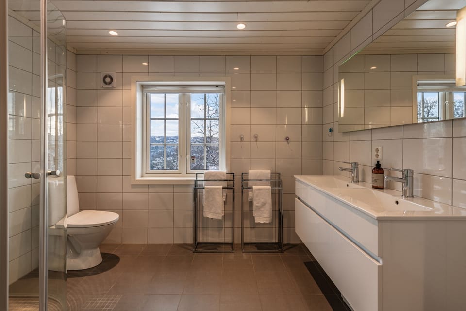 Spacious bathroom with a large window, double sink, walk-in shower, and modern white tiles throughout.