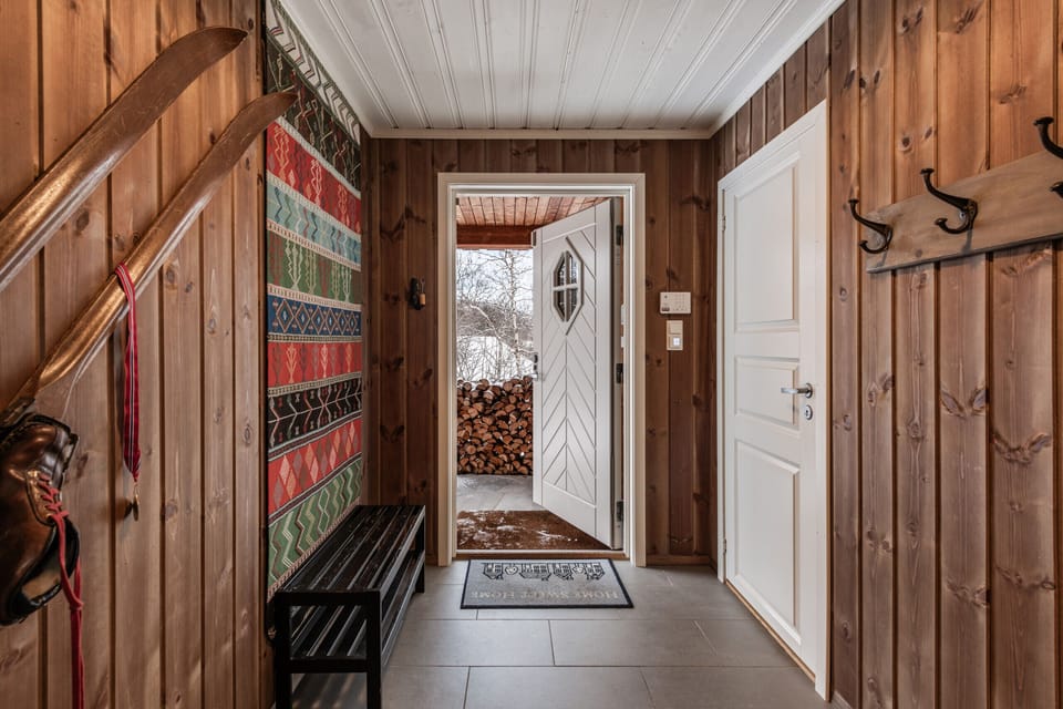 Inviting entryway with vintage skis on the wall, colorful woven tapestry, coat hooks, and a bench.