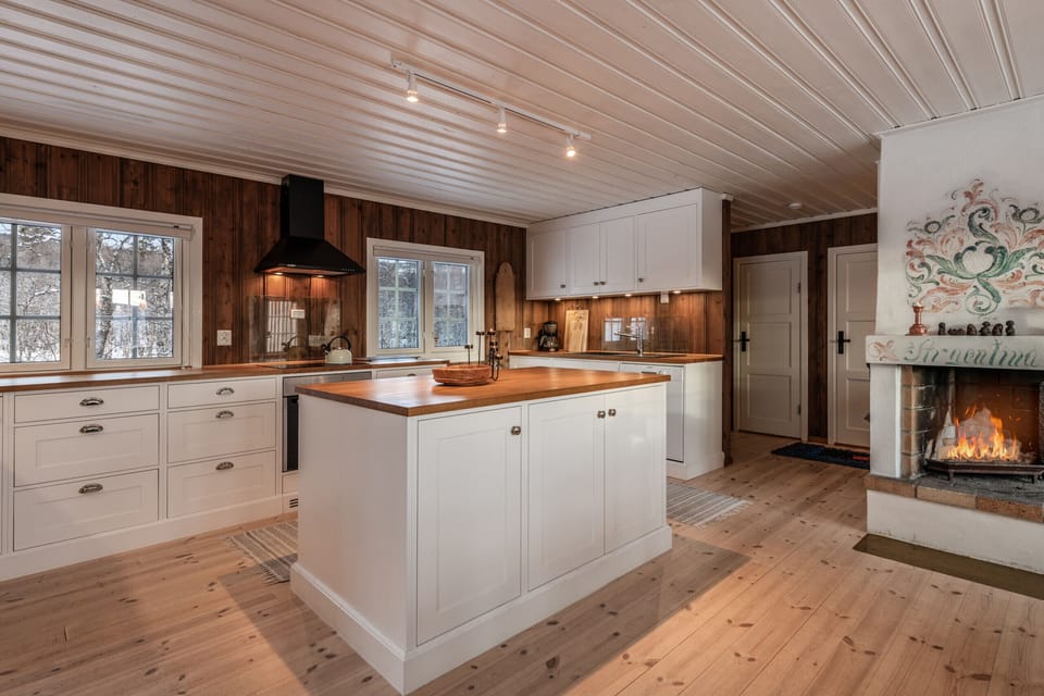 Bright kitchen with white cabinets, wooden countertops, a central island, and a cozy fireplace in the corner.