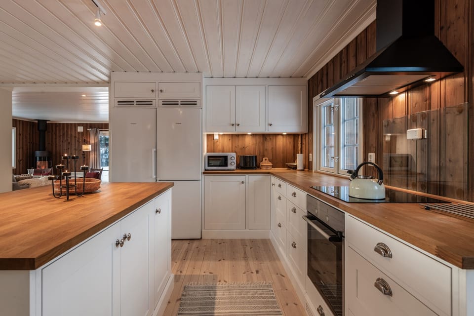 Bright, well-equipped kitchen featuring white cabinets, double-door fridge, wood countertops, modern appliances, and a large island for cooking and gathering.