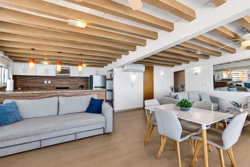 Spacious open-plan room combining a large dining table setup, a long grey sofa, and a modern kitchen with wooden finishes.
