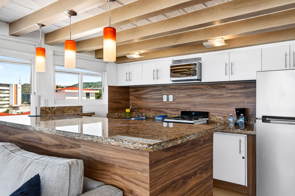 Sleek kitchen workspace featuring rich granite counters, warm wood paneling, white cabinetry, and stylish orange pendant lights.
