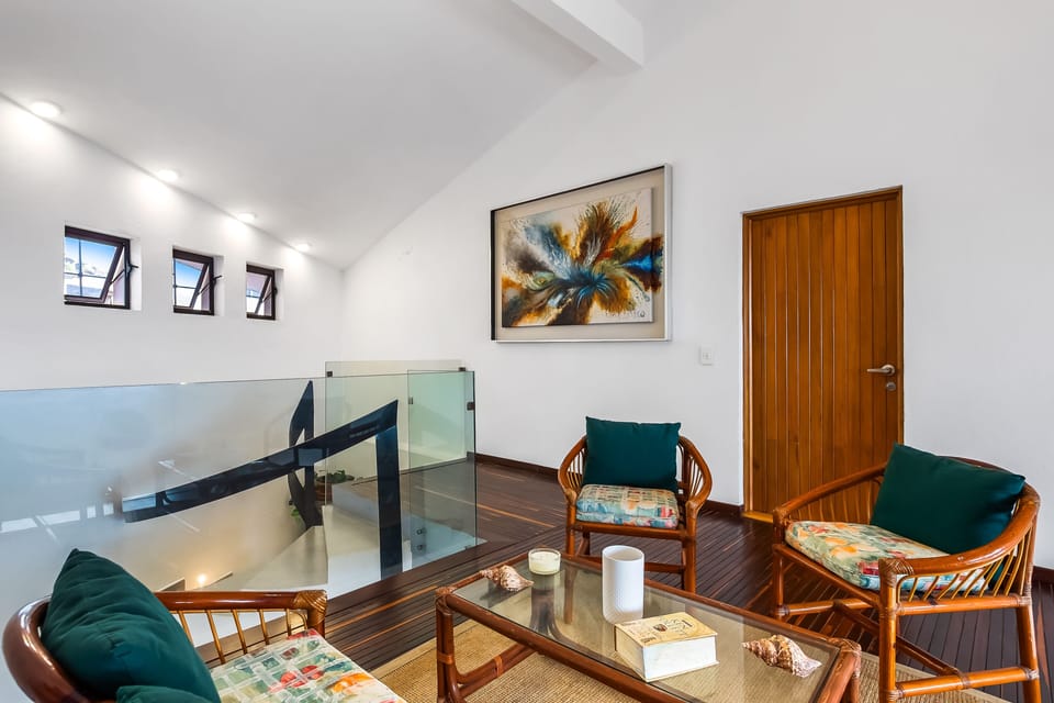 Spacious second-floor landing area featuring a comfortable seating arrangement, glass railings, a modern staircase, and unique sloped ceiling architecture.