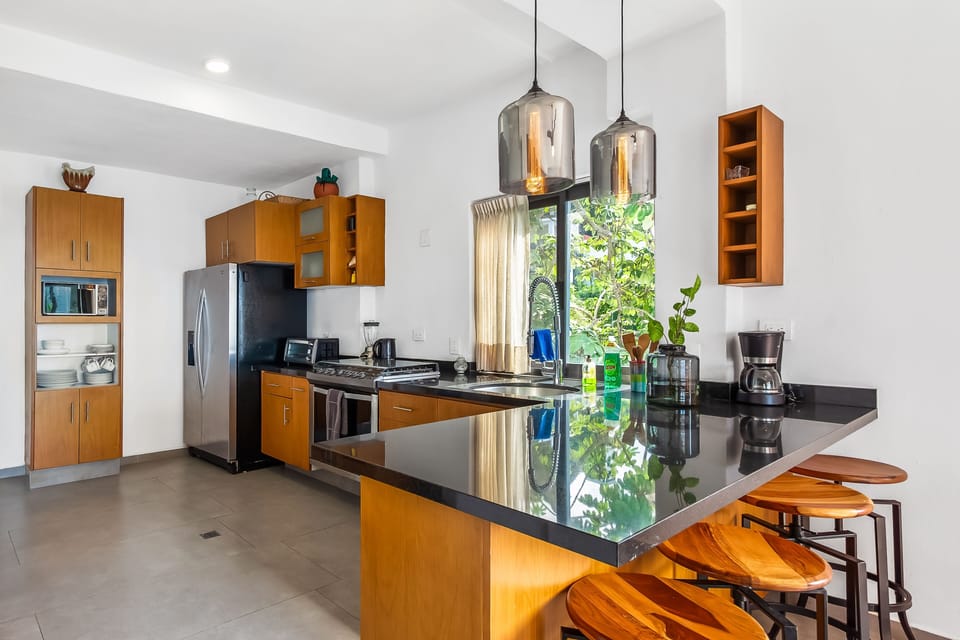 Bright kitchen featuring wooden cabinetry, dark granite countertops, stainless steel appliances, and a breakfast bar with matching stools.