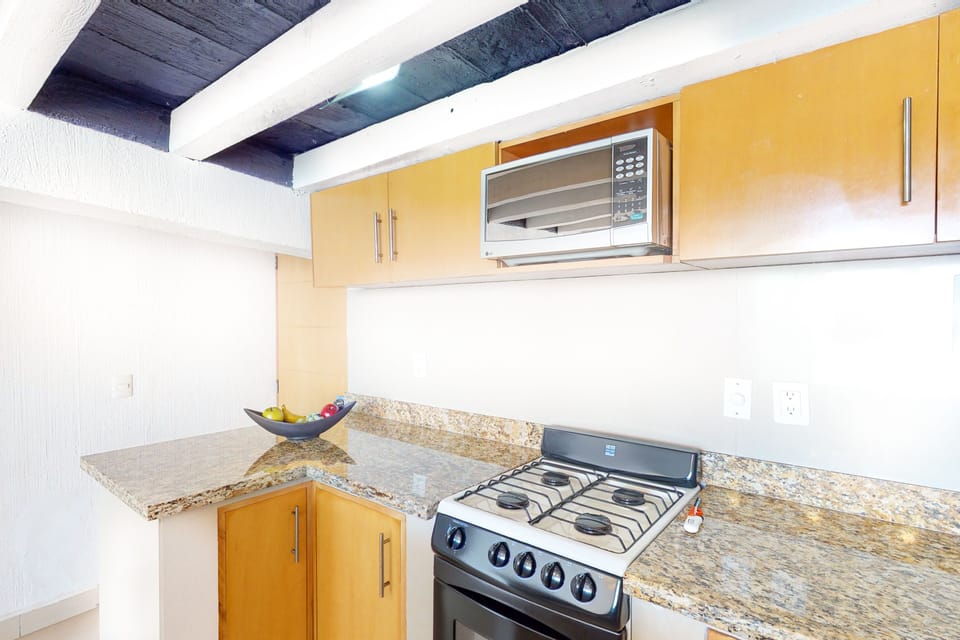 Close-up view highlighting a modern gas range stove, a built-in microwave, and polished granite countertops under a beamed ceiling.