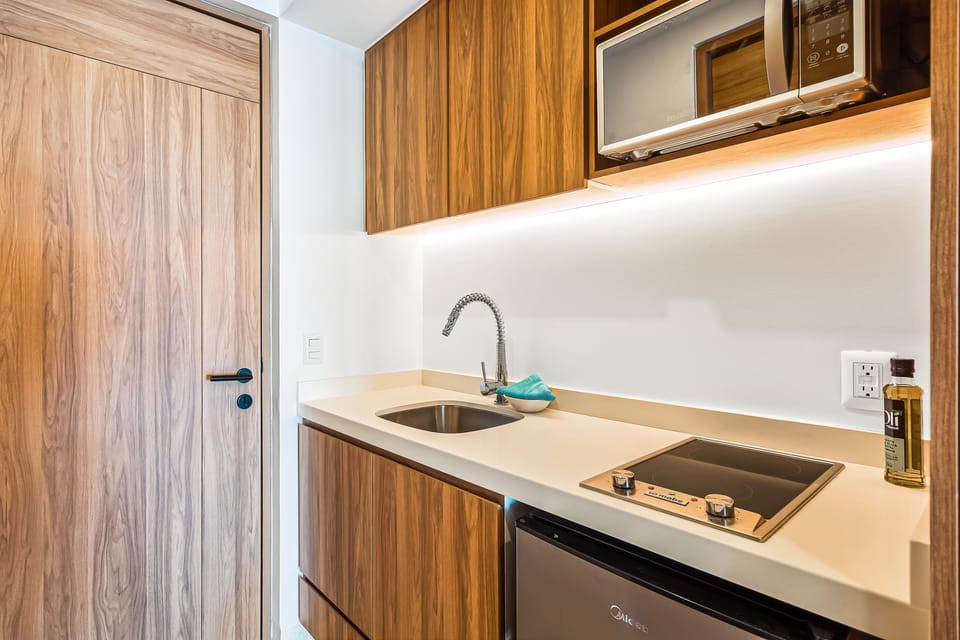 Modern kitchenette equipped with an under-mount sink, integrated electric cooktop, and under-cabinet LED strip lighting.