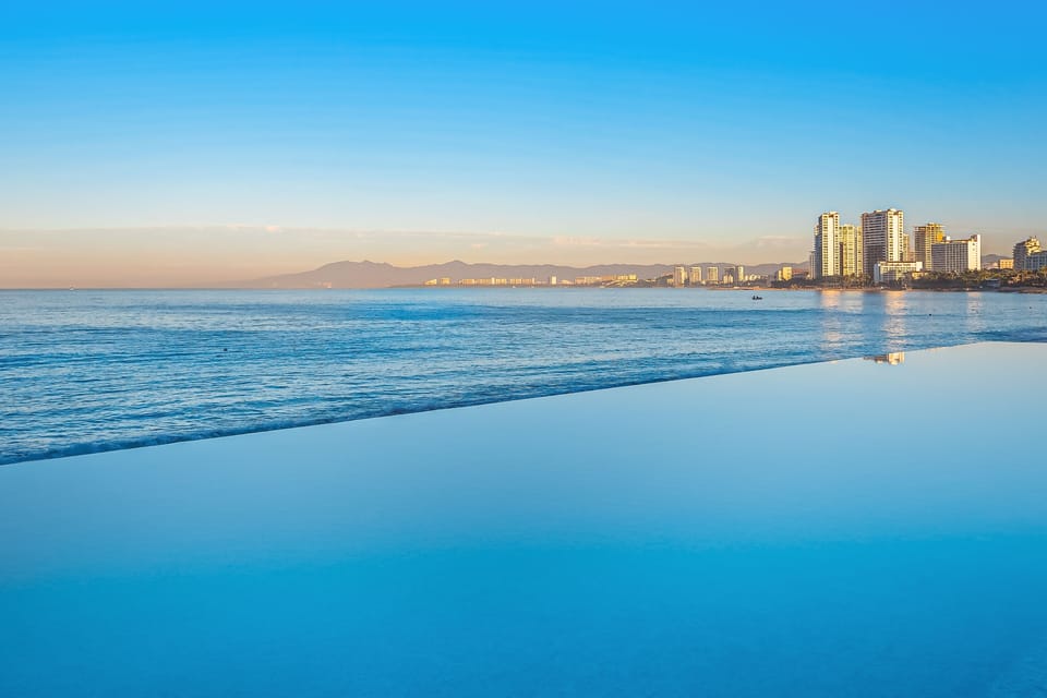 Shimmering infinity pool edge blending seamlessly into the ocean with distant city buildings along the coast.