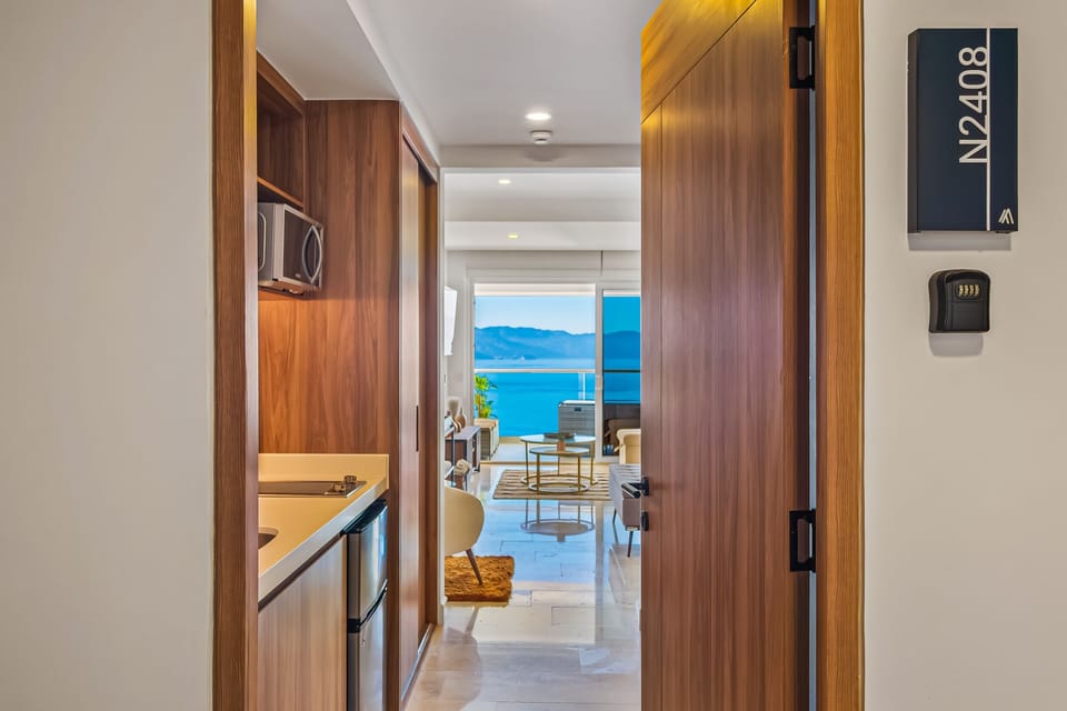 Looking past the open front door down a long interior hallway past the kitchen into the bright studio living space.