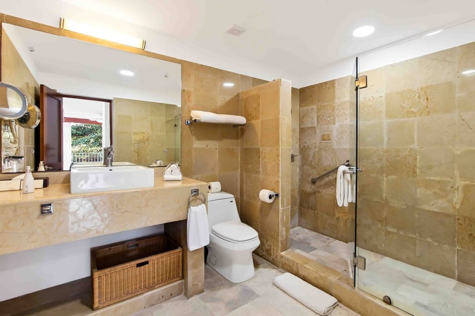 Bathroom with stone tiles, a glass shower enclosure, vanity, and a woven laundry basket.