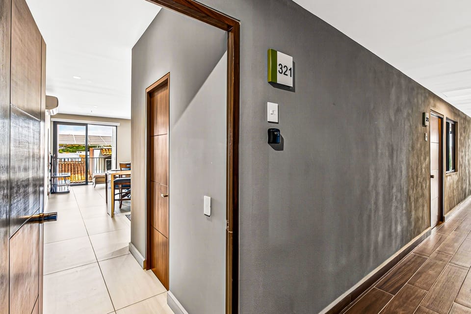 A view from the building's corridor looking into the bright apartment entryway, featuring a textured grey accent wall and warm wood trim.