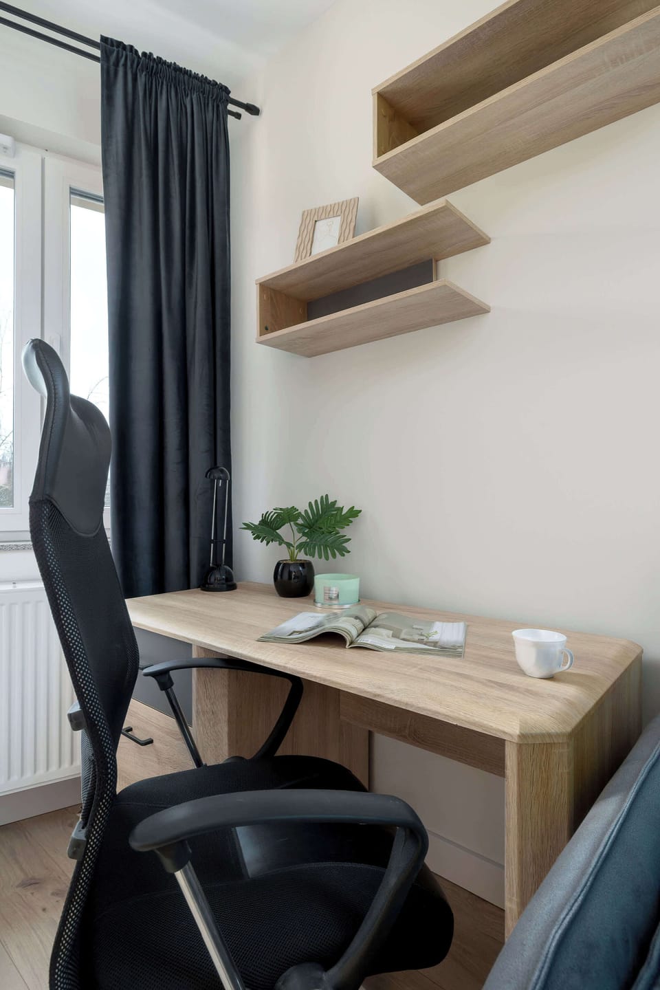 A functional home office corner equipped with a clean desk, an ergonomic black chair, and minimalist wall shelving. This dedicated nook is ideal for remote work or study.