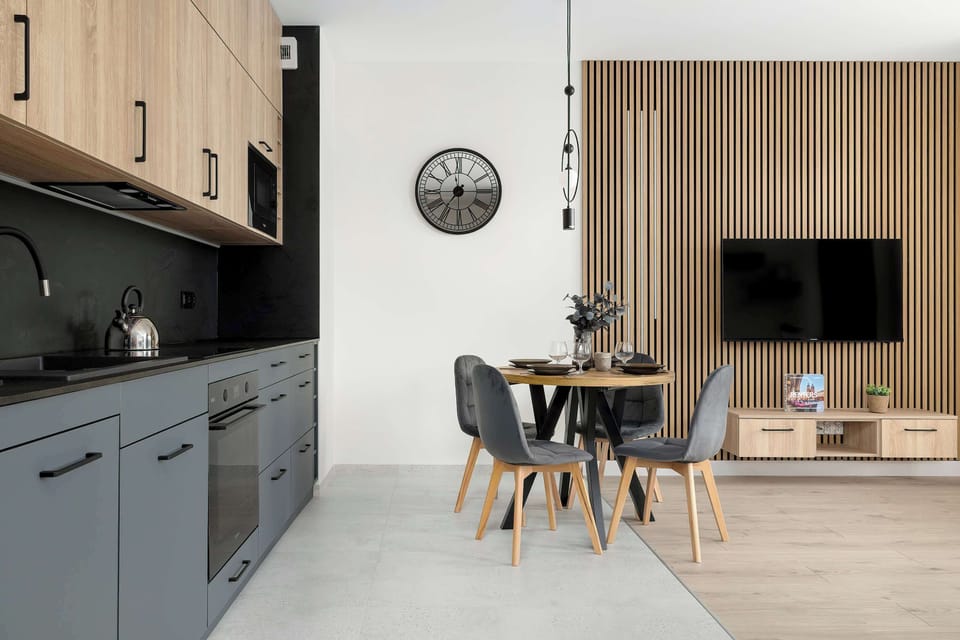 A perspective of the kitchen looking toward the dining area, featuring modern appliances and a wall-mounted television. The design emphasizes a seamless flow between cooking and living zones.