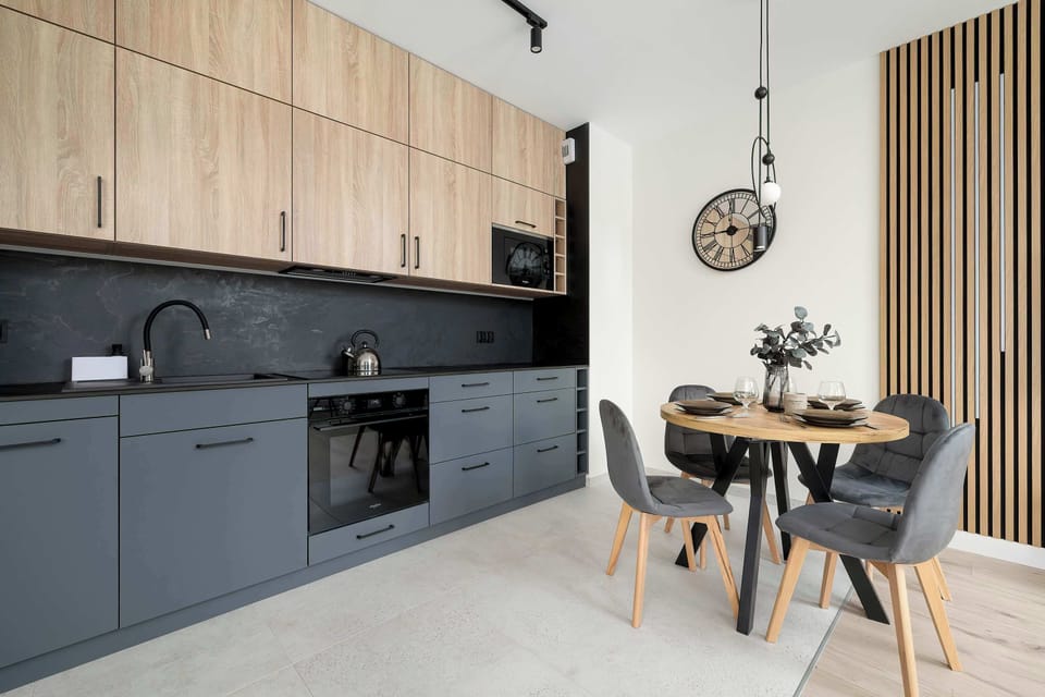 A sleek, open-plan kitchen with grey cabinetry, wooden accents, and a round dining table for four. This functional space combines modern design with practical dining arrangements.