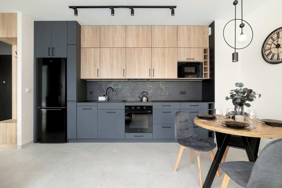 A wide-angle view of the kitchen suite, showcasing a large black refrigerator and streamlined cabinetry. The layout is designed for maximum efficiency and modern style.