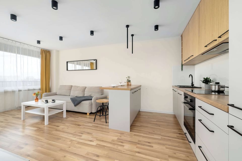 A view from the living room toward the kitchen, showcasing the functional layout of the space and the harmony of white, wood, and black lighting details.
