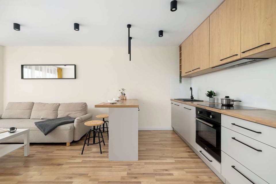 A bright living room with a comfortable sofa and a view of the kitchenette, highlighting the consistency of the finishing materials and the wood-textured floor.