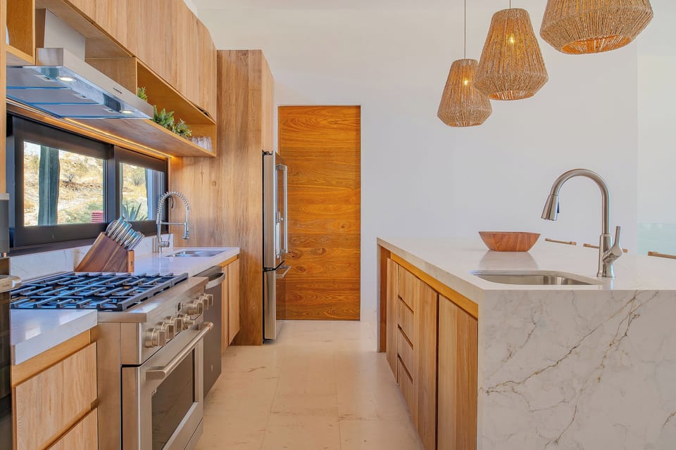 Your gourmet kitchen awaits with warm wood cabinetry, marble counters, and woven pendant lights creating the perfect culinary retreat.