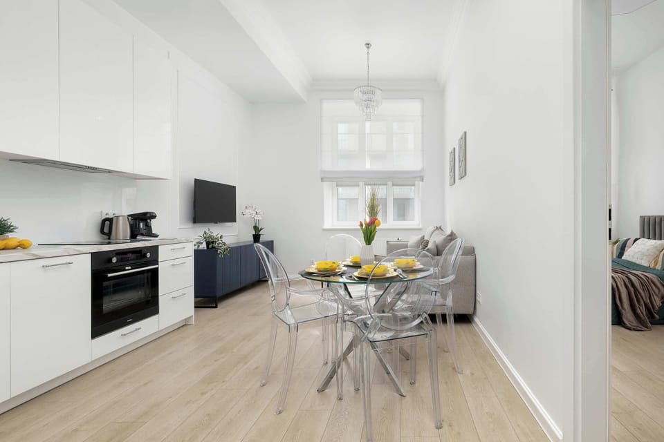 An wide-angle shot looking down a hallway with a modern, L-shaped kitchen along one wall. The light wood flooring flows through to a living area in the background.